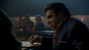 Movie still from “The Sopranos” (1999), created by David Chase – A man sitting at a table writing on a piece of paper; Medium shot, Low angle