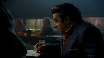 Movie still from “The Sopranos” (1999), created by David Chase – A man in a suit writing on a piece of paper; Medium shot, Over the shoulder angle