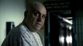 Movie still from “The Sopranos” (1999), created by David Chase – An older bald man wearing a hospital gown and ear buds; Close Up shot, Low angle