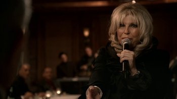 Movie still from “The Sopranos” (1999), created by David Chase – A woman holding a microphone in a room; Close Up shot, Over the shoulder angle