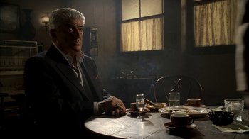 Movie still from “The Sopranos” (1999), created by David Chase – A man sitting at a table with a cup of coffee; Medium shot, Low angle