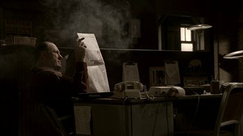 Movie still from “The Sopranos” (1999), created by David Chase – A man sitting at a table with papers in front of him; Medium shot, Low angle