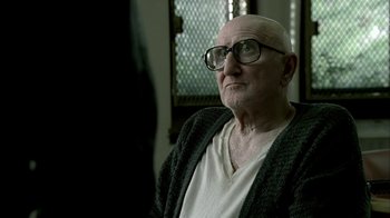 Movie still from “The Sopranos” (1999), created by David Chase – An old man wearing glasses sitting in a chair; Close Up shot, Over the shoulder angle
