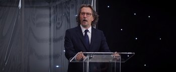 Movie still from “The Space Between Us” (2017), directed by Peter Chelsom – A man in a suit and tie standing at a lectern; Medium shot, Over the shoulder angle