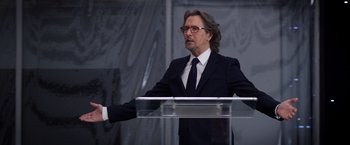 Movie still from “The Space Between Us” (2017), directed by Peter Chelsom – A man in a suit and tie standing at a podium; Medium shot, Over the shoulder angle
