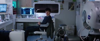 Movie still from “The Space Between Us” (2017), directed by Peter Chelsom – A man sitting in a chair in front of a computer desk; Medium shot, High angle