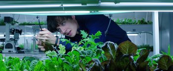 Movie still from “The Space Between Us” (2017), directed by Peter Chelsom – A man looking at plants under a grow light; Close Up shot, Low angle