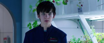 Movie still from “The Space Between Us” (2017), directed by Peter Chelsom – A young man in a blue jacket standing in front of a plant; Close Up shot, Over the shoulder angle