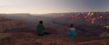 Movie still from “The Space Between Us” (2017), directed by Peter Chelsom – A man and a woman sitting on the side of a cliff; Extreme Wide shot, High angle