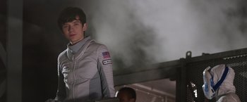 Movie still from “The Space Between Us” (2017), directed by Peter Chelsom – A man in a spacesuit standing in front of a smoke stack; Medium shot, Over the shoulder angle