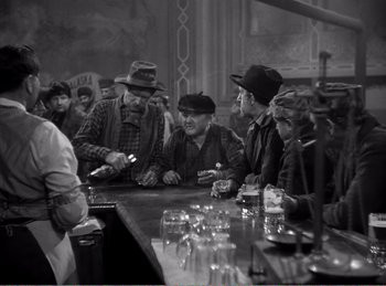 Movie still from “The Spoilers” (1942), directed by Ray Enright – A black and white photo of men sitting at a bar; Medium shot, High angle