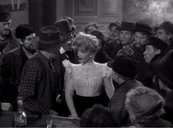 Movie still from “The Spoilers” (1942), directed by Ray Enright – An old black and white photo of a woman in a crowd; Medium shot, Over the shoulder angle