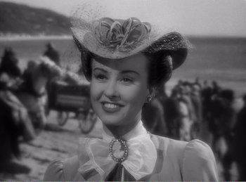 Movie still from “The Spoilers” (1942), directed by Ray Enright – A woman wearing a hat and a bow tie; Close Up shot, Over the shoulder angle