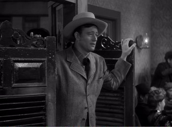 Movie still from “The Spoilers” (1942), directed by Ray Enright – A black and white photo of a man wearing a hat; Medium shot, Over the shoulder angle