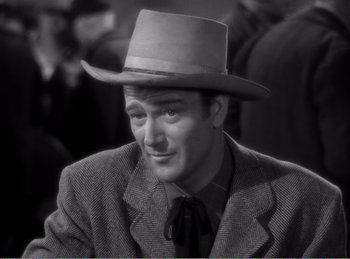 Movie still from “The Spoilers” (1942), directed by Ray Enright – A black and white photo of a man wearing a hat; Close Up shot, Over the shoulder angle