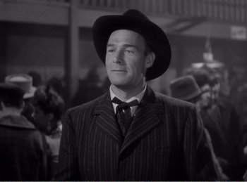 Movie still from “The Spoilers” (1942), directed by Ray Enright – A black and white photo of a man in a suit and a hat; Medium shot, Low angle