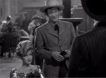 Movie still from “The Spoilers” (1942), directed by Ray Enright – A man and a woman are standing in front of a crowd; Medium shot, Over the shoulder angle