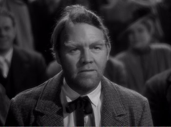 Movie still from “The Spoilers” (1942), directed by Ray Enright – A man in a suit and tie in a black and white photo; Close Up shot, Over the shoulder angle