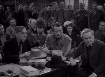 Movie still from “The Spoilers” (1942), directed by Ray Enright – A group of people sitting around a table; Medium shot, High angle