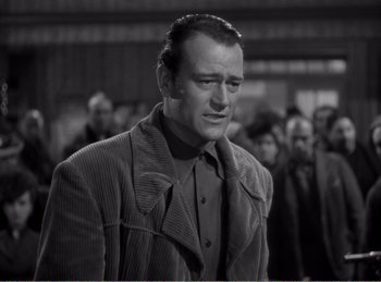 Movie still from “The Spoilers” (1942), directed by Ray Enright – A black and white photo of a man in a crowd; Medium shot, Low angle