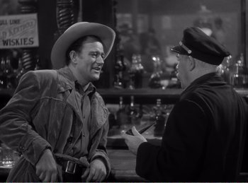Movie still from “The Spoilers” (1942), directed by Ray Enright – A man wearing a cowboy hat talking to another man; Medium shot, Over the shoulder angle