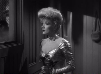 Movie still from “The Spoilers” (1942), directed by Ray Enright – A black and white photo of a woman in a silver dress; Medium shot, Low angle