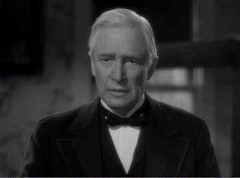 Movie still from “The Spoilers” (1942), directed by Ray Enright – An older man wearing a suit and bow tie; Close Up shot, Over the shoulder angle