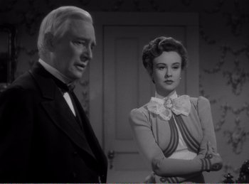 Movie still from “The Spoilers” (1942), directed by Ray Enright – An older man standing next to an older woman in a room; Medium shot, Over the shoulder angle