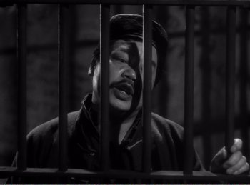 Movie still from “The Spoilers” (1942), directed by Ray Enright – A man with a beard and mustache is behind bars; Medium shot, High angle