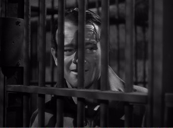 Movie still from “The Spoilers” (1942), directed by Ray Enright – A black and white photo of a man behind bars; Close Up shot, High angle