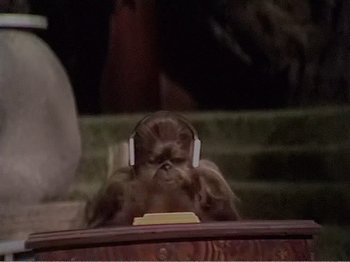 Movie still from “The Star Wars Holiday Special” (1978), directed by Steve Binder – A monkey sitting in front of some stairs wearing headphones; Medium shot, High angle