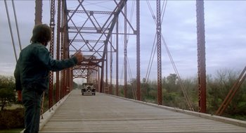 Movie still from “The Stunt Man” (1980), directed by Richard Rush – A man is reaching out to a car on a bridge; Extreme Wide shot, Low angle