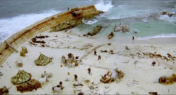 Movie still from “The Stunt Man” (1980), directed by Richard Rush – An aerial view of people on a beach near the ocean; Extreme Wide shot, High angle
