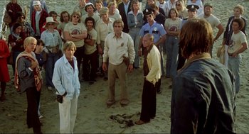 Movie still from “The Stunt Man” (1980), directed by Richard Rush – A group of people standing on top of a sandy beach; Wide shot, High angle