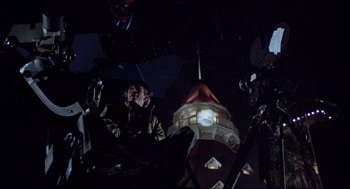 Movie still from “The Stunt Man” (1980), directed by Richard Rush – A man is sitting in front of a building at night; Wide shot, Low angle