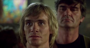Movie still from “The Stunt Man” (1980), directed by Richard Rush – A man with long blonde hair is looking at the camera while another man stands next to him; Close Up shot, Low angle