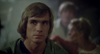 Movie still from “The Stunt Man” (1980), directed by Richard Rush – A man with long blonde hair is looking at the camera; Close Up shot, Over the shoulder angle