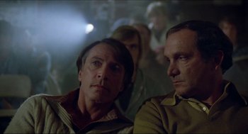 Movie still from “The Stunt Man” (1980), directed by Richard Rush – Two men sitting next to each other in front of a crowd; Close Up shot, Over the shoulder angle