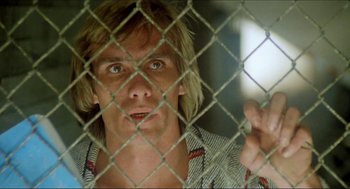Movie still from “The Stunt Man” (1980), directed by Richard Rush – A man looking through a chain link fence; Close Up shot, Low angle