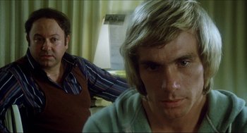 Movie still from “The Stunt Man” (1980), directed by Richard Rush – A man sitting next to another man in front of a lamp; Close Up shot, Over the shoulder angle