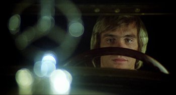 Movie still from “The Stunt Man” (1980), directed by Richard Rush – A young man driving a car at night with lights in the background; Close Up shot, Low angle