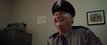 Movie still from “The Sugarland Express” (1974), directed by Steven Spielberg – A man in a police uniform smiling for the camera; Close Up shot, Low angle