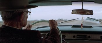 Movie still from “The Sugarland Express” (1974), directed by Steven Spielberg – An older man driving a car with his hands on the steering wheel; Medium shot, Over the shoulder angle