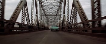 Movie still from “The Sugarland Express” (1974), directed by Steven Spielberg – A car is driving on a bridge over a river; Extreme Wide shot, Low angle