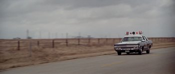 Movie still from “The Sugarland Express” (1974), directed by Steven Spielberg – A car driving down a road near a fence; Wide shot, Low angle