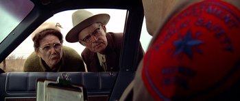 Movie still from “The Sugarland Express” (1974), directed by Steven Spielberg – An older man wearing a hat looking into a car mirror; Medium shot, Over the shoulder angle