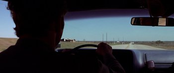 Movie still from “The Sugarland Express” (1974), directed by Steven Spielberg – A man driving a car on a road; Wide shot, Over the shoulder angle