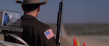 Movie still from “The Sugarland Express” (1974), directed by Steven Spielberg – A man holding a rifle with an american flag patch on it; Medium shot, Low angle
