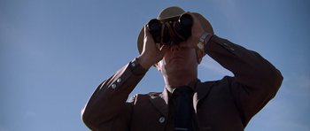 Movie still from “The Sugarland Express” (1974), directed by Steven Spielberg – A man looking through binoculars while wearing a hat; Medium shot, Low angle