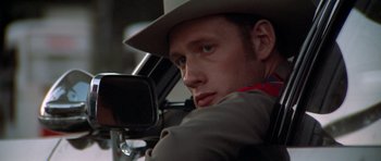 Movie still from “The Sugarland Express” (1974), directed by Steven Spielberg – A man in a hat and a jacket looking in the side mirror of a car; Close Up shot, Over the shoulder angle